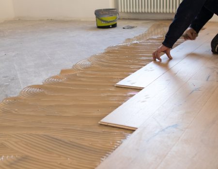 Renovation of an apartment, skilled worker uses a plastic hammer when installing pre-finished interlocking parquet. Laying with brown glue on an existing floor. Installation of oak colored parquet